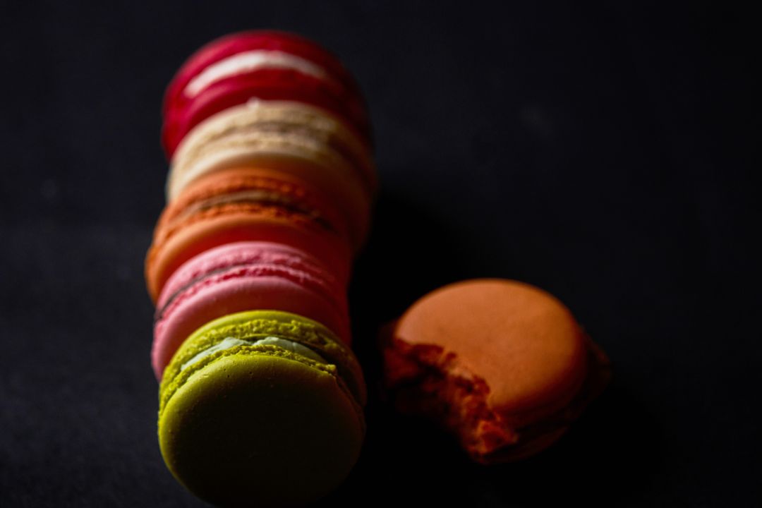 Colorful French macarons stacking on dark background featuring bitten orange macaron