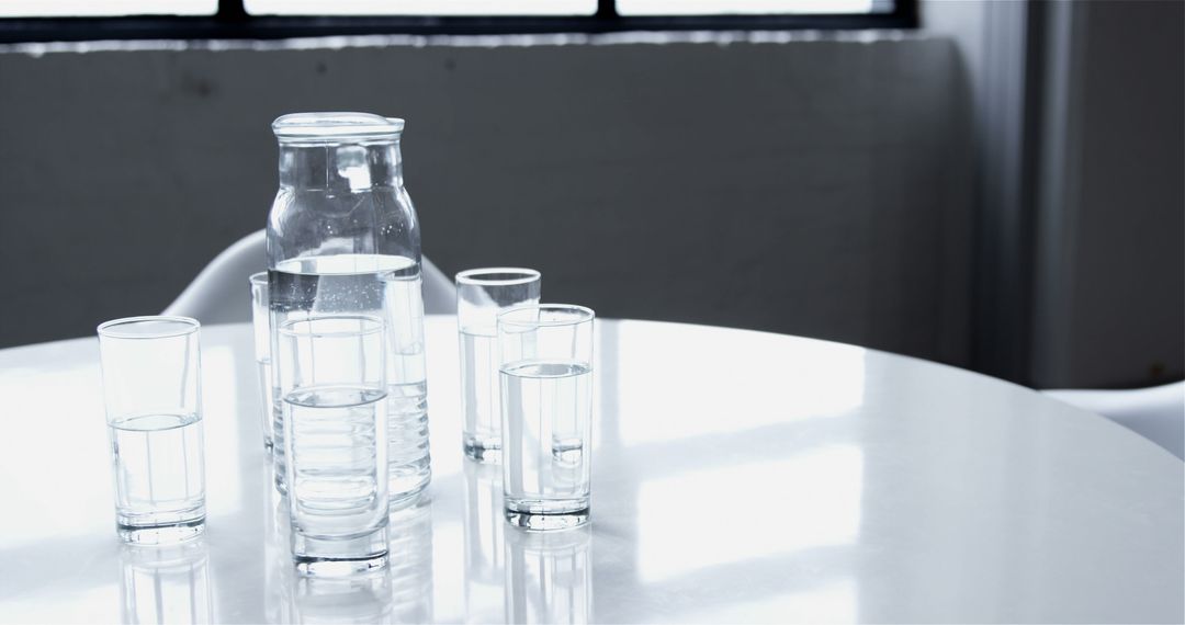 Glass Jug with Water and Drinking Glasses on Round White Table in Minimalist Setting - Free Images, Stock Photos and Pictures on Pikwizard.com