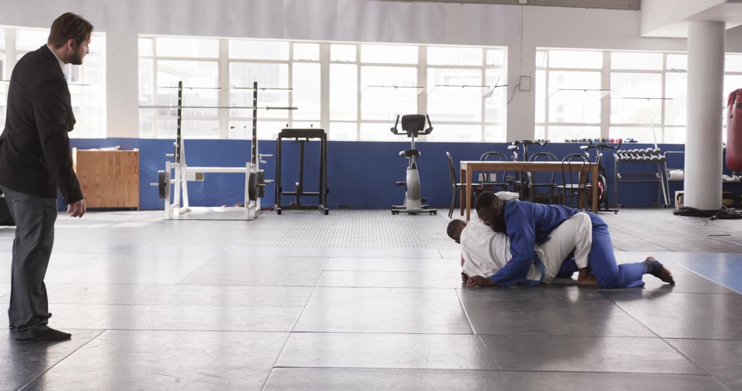 Coach Overseeing Grappling Students in Well-Equipped Gym
