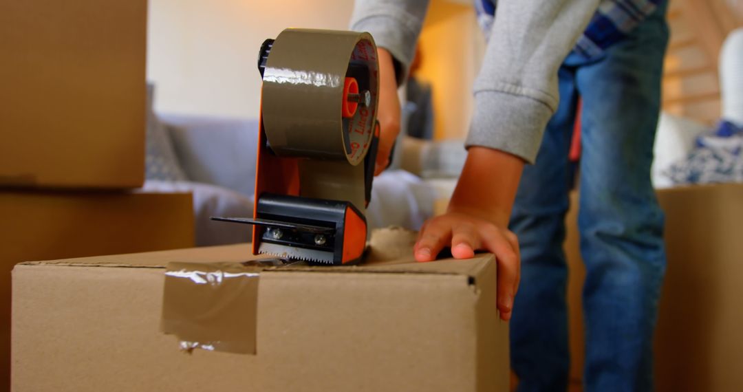 Person Sealing Cardboard Box with Tape Dispenser in Living Room - Free Images, Stock Photos and Pictures on Pikwizard.com