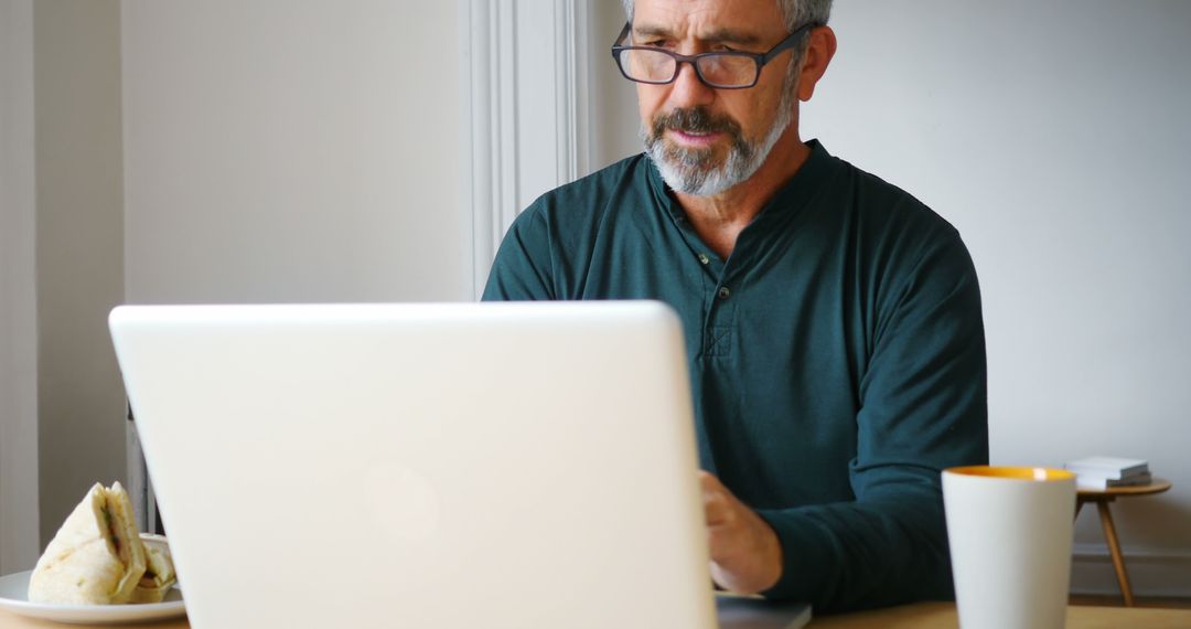 Mature Man Working on Laptop at Home with Coffee and Snack - Free Images, Stock Photos and Pictures on Pikwizard.com