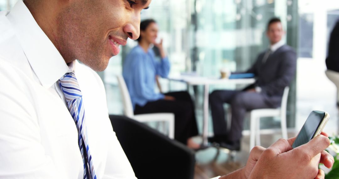 Businessman texting in modern office building with colleagues interacting in background - Free Images, Stock Photos and Pictures on Pikwizard.com