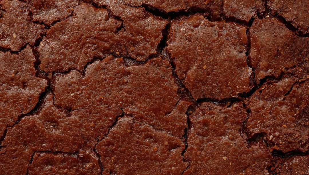 Cracked Chocolate Brownie Surface Macro Texture Showing Glossy Crust, Fissures, Crumbs