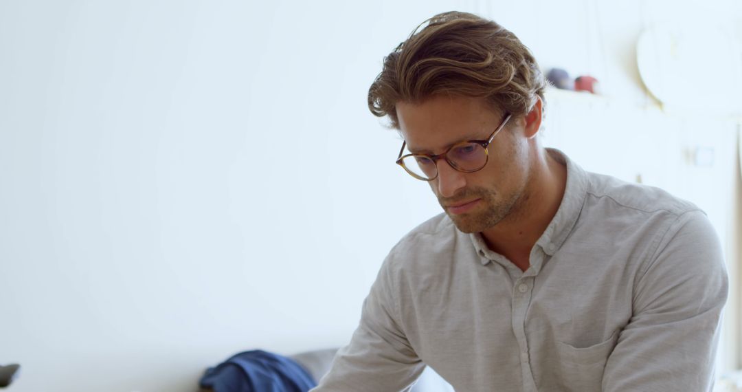 Thoughtful young man in glasses focused on work at home - Free Images, Stock Photos and Pictures on Pikwizard.com