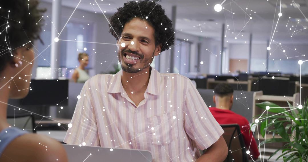 Smiling man collaborating in modern open-plan office with laptop and digital network overlay