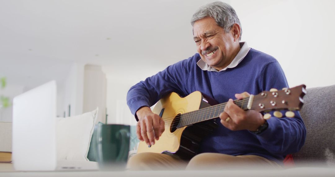 Image of smiling senior biracial man using laptop and playing acoustic guitar at home - Free Images, Stock Photos and Pictures on Pikwizard.com