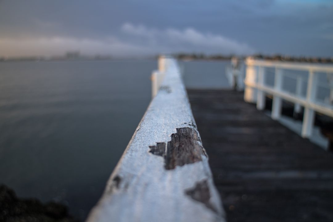 Rustic Wooden Pier Extending Over Tranquil Water under Overcast Sky - Free Images, Stock Photos and Pictures on Pikwizard.com