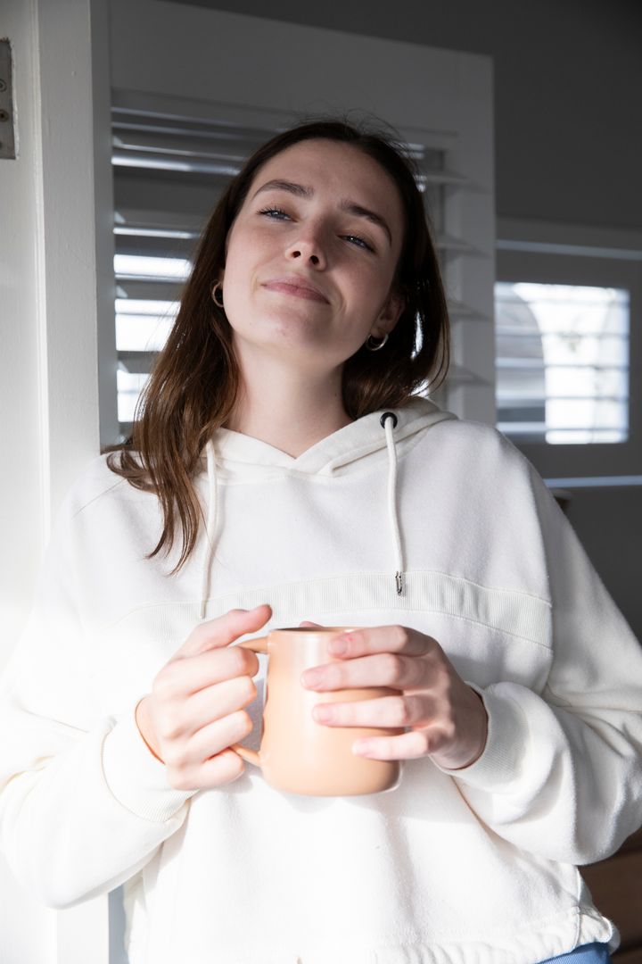 Serene Woman Enjoying Morning Sunlight Near Window with Mug