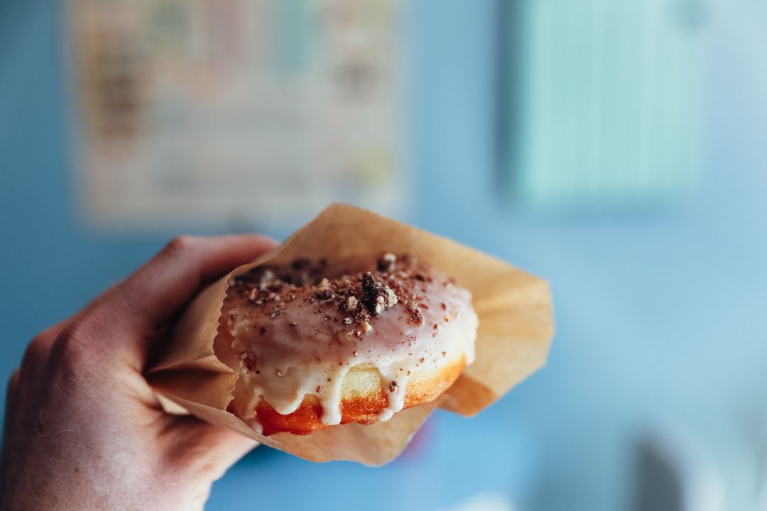 Close Up of a Hand Holding a Glazed Doughnut with Crumbs