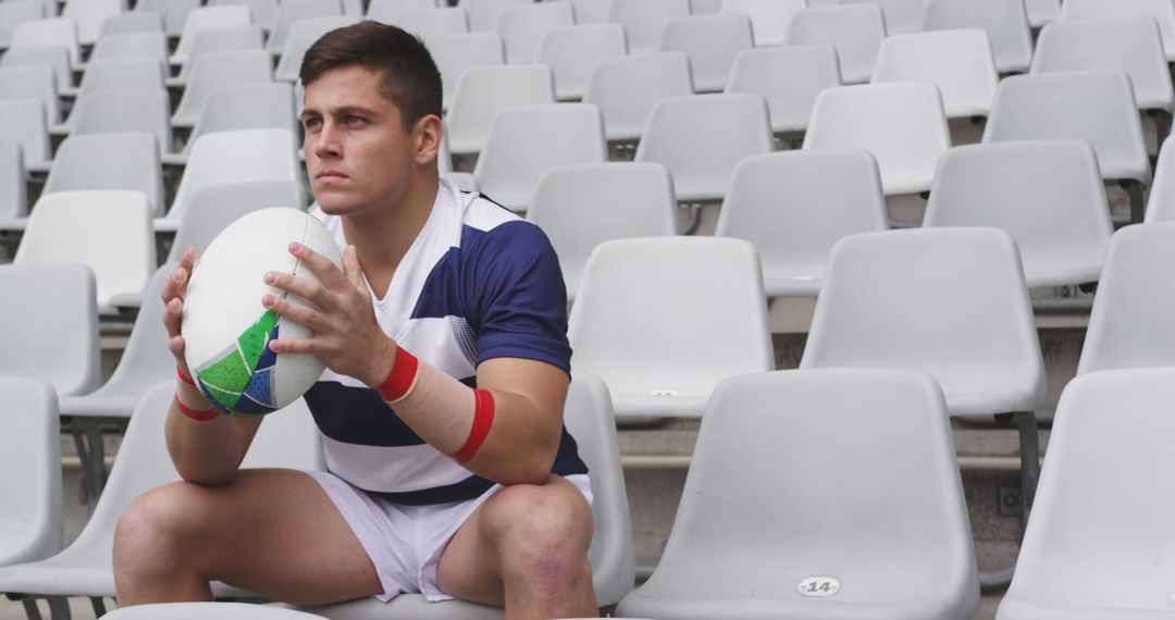 Rugby player sitting in stadium holding ball focused on game - Free Images, Stock Photos and Pictures on Pikwizard.com