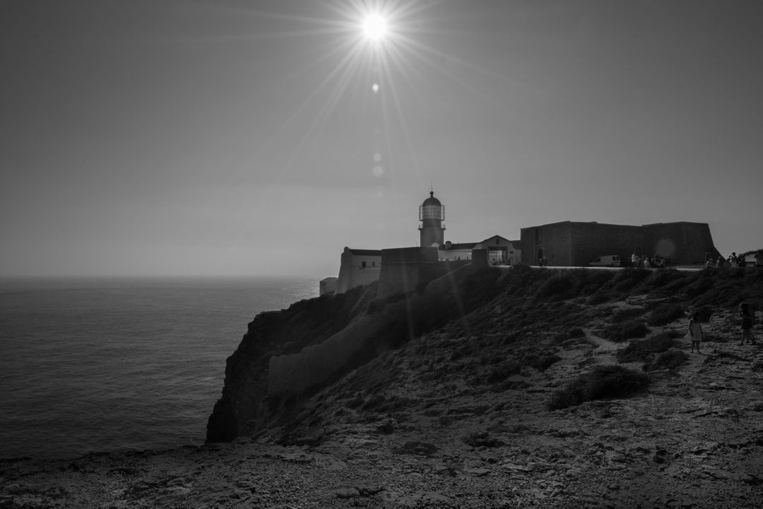 Sunlit Cliffside Fortress with Lighthouse Overlooking Ocean in Black and White - Free Images, Stock Photos and Pictures on Pikwizard.com