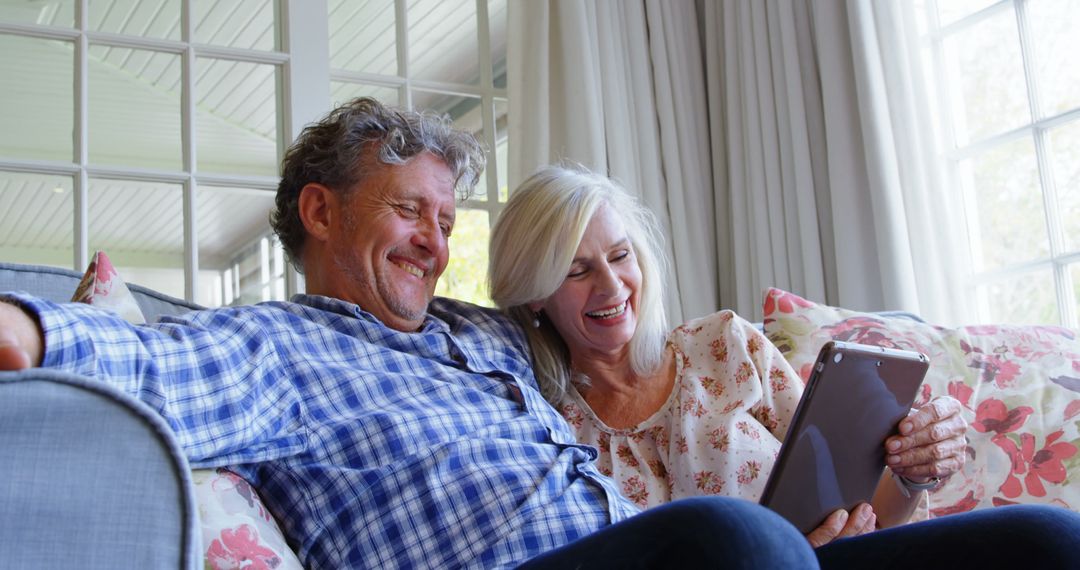 Happy Senior Couple Enjoying Tablet on Sofa at Home