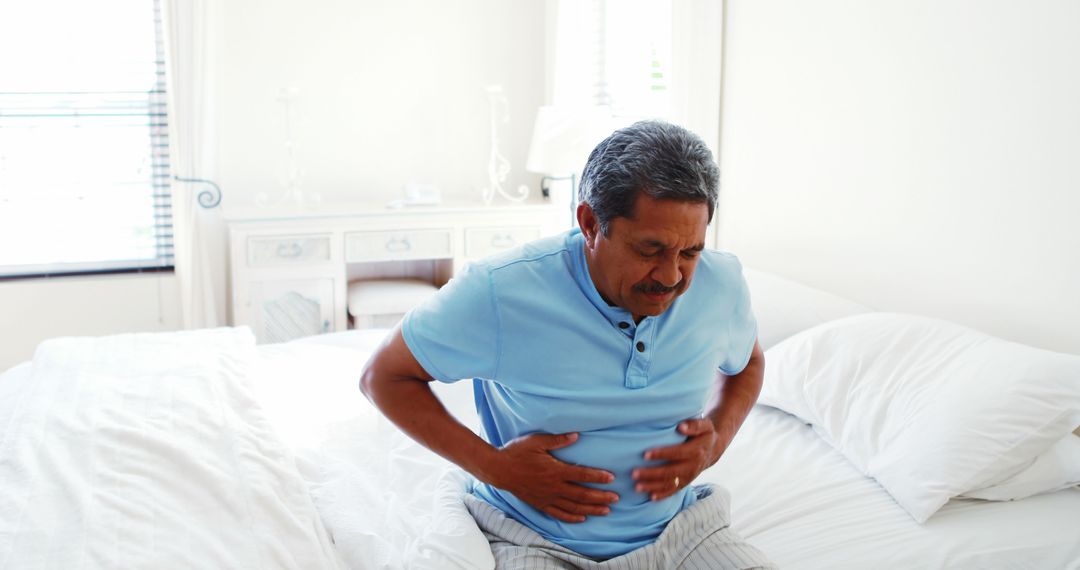 Senior Man Suffering from Stomach Pain Seated on Bed - Free Images, Stock Photos and Pictures on Pikwizard.com