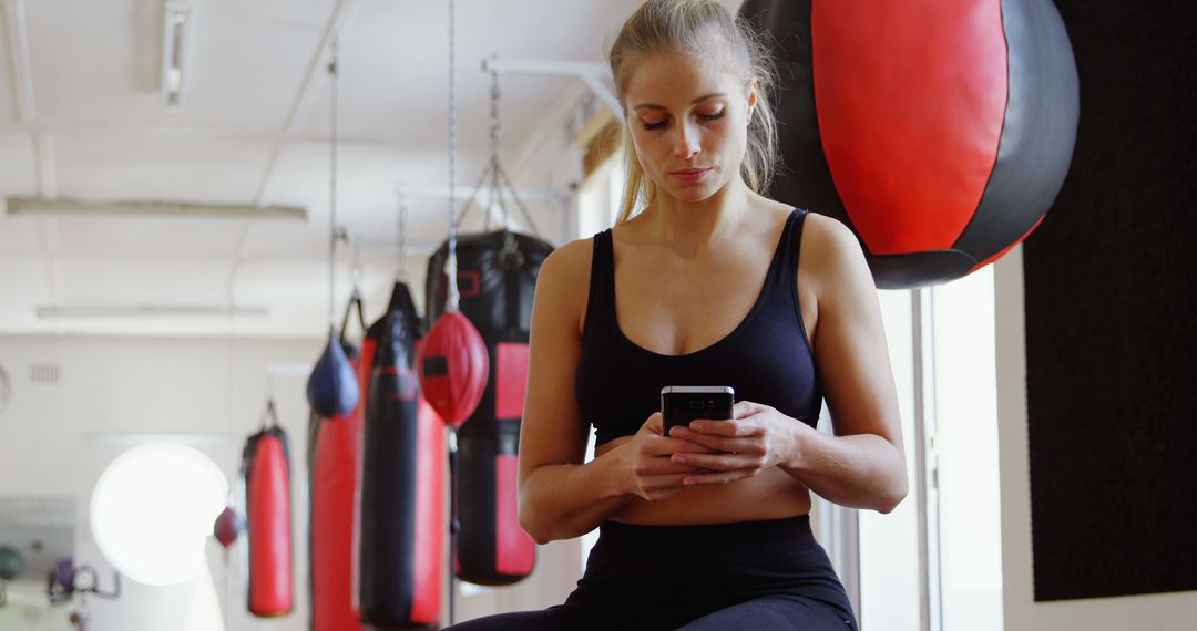 Focused Woman Checking Phone in Modern Gym with Punching Bags - Free Images, Stock Photos and Pictures on Pikwizard.com