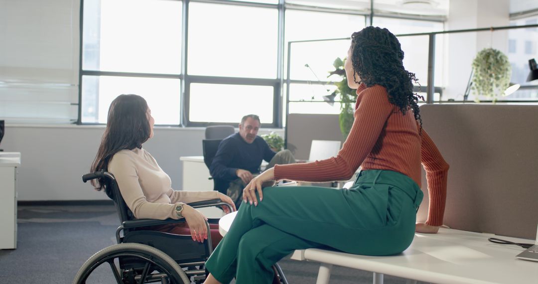 Diverse team collaborating around round table with wheelchair in modern open-plan office