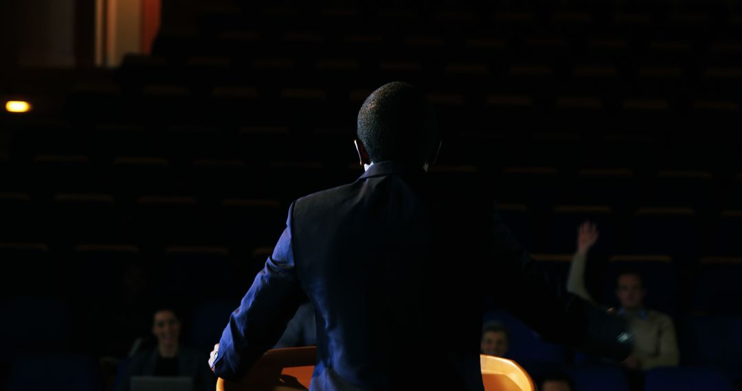 Confident Speaker Giving a Presentation in Dark Auditorium - Free Images, Stock Photos and Pictures on Pikwizard.com