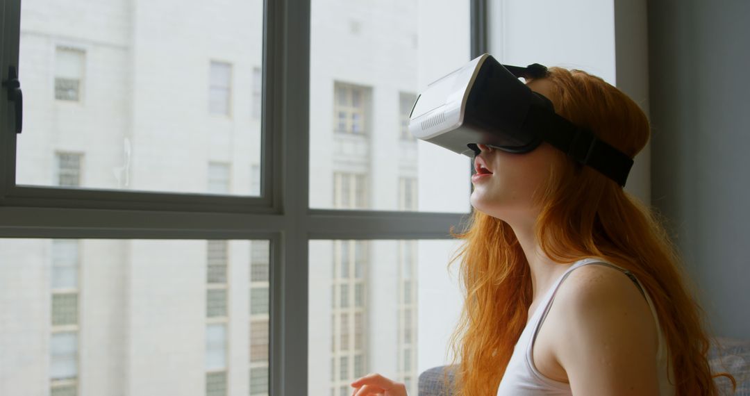 Redheaded Woman Experiencing Virtual Reality Indoors Near Window - Free Images, Stock Photos and Pictures on Pikwizard.com