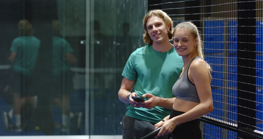 Couple Relaxing on Padel Court Holding Smartphone and Racket