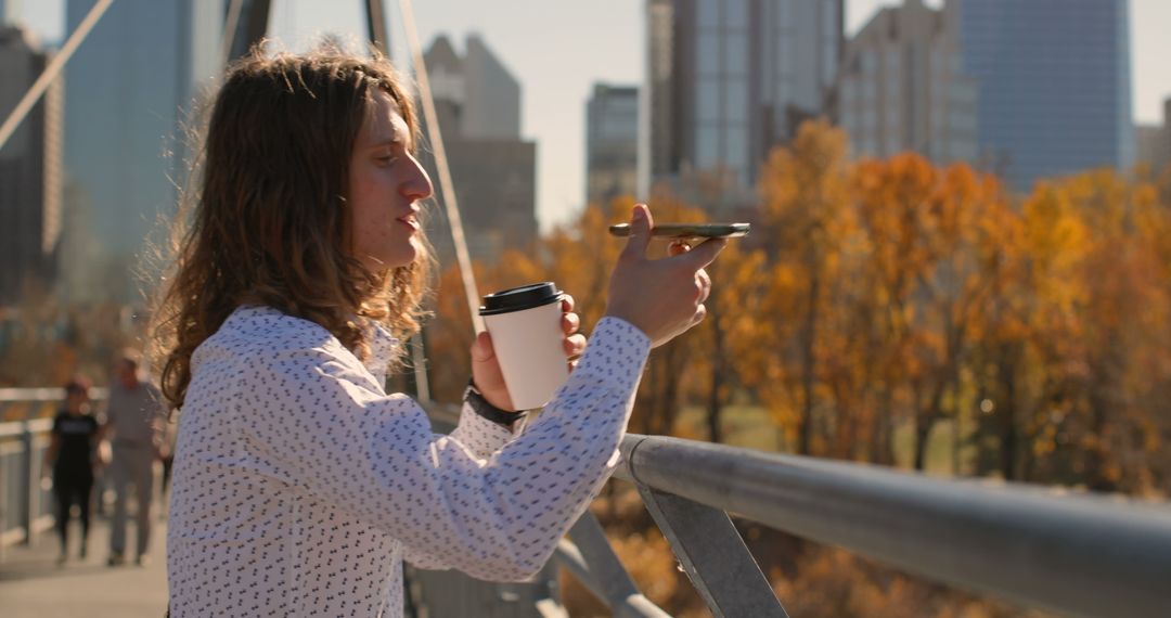 Young Man Enjoying Autumn Day with Coffee and Smartphone on Urban Bridge - Free Images, Stock Photos and Pictures on Pikwizard.com