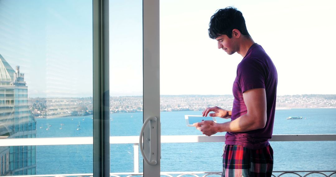 Young man using tablet on balcony overlooking bay, morning - Free Images, Stock Photos and Pictures on Pikwizard.com