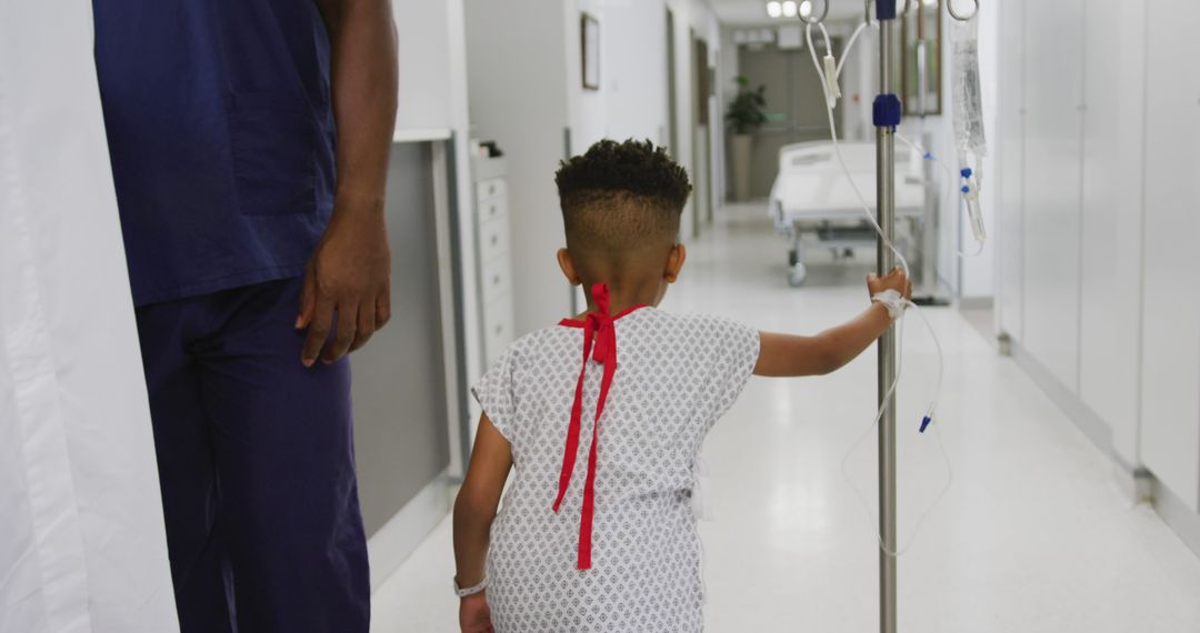 Rear view of african american boy patient walking and holding drip stand in hospital corridor - Free Images, Stock Photos and Pictures on Pikwizard.com