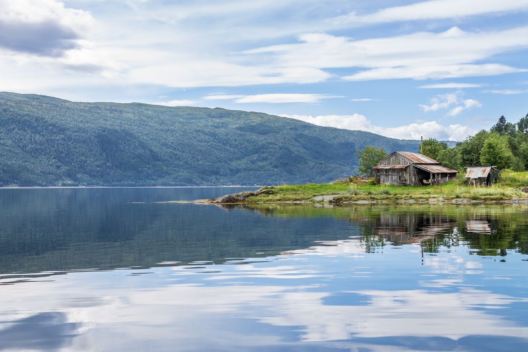Rustic boathouse on tranquil fjord with mountain reflection and calm water