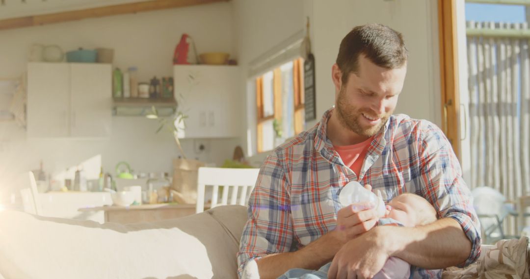 Smiling Father Feeding Infant at Home in Sunlit Living Room - Free Images, Stock Photos and Pictures on Pikwizard.com