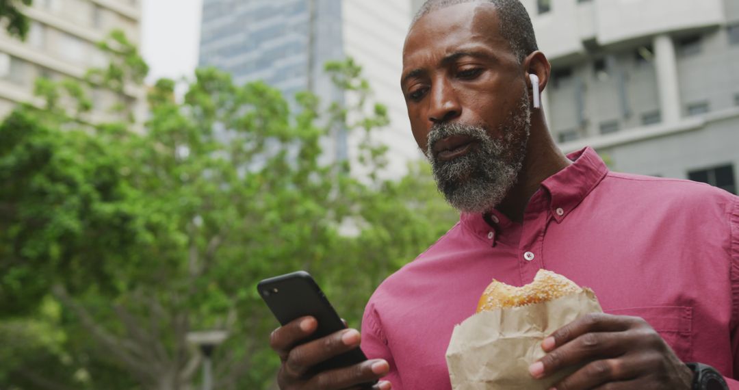 Mature Man Eating Sandwich and Using Smartphone in Urban Setting - Free Images, Stock Photos and Pictures on Pikwizard.com