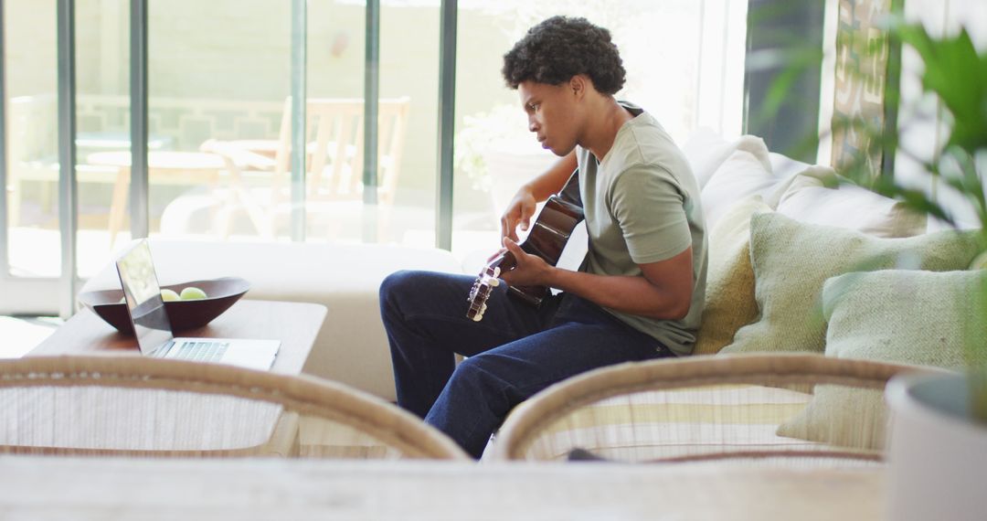 Man Playing Guitar and Using Laptop at Home