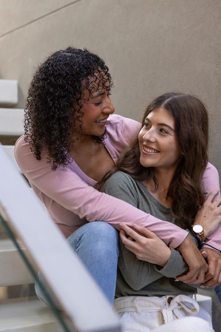 Diverse Young Female Couple Embracing on Steps Smiling Joyfully