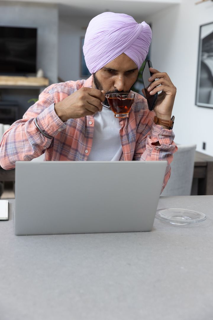Man in Lavender Turban Multitasking at Home Workspace with Laptop and Tea