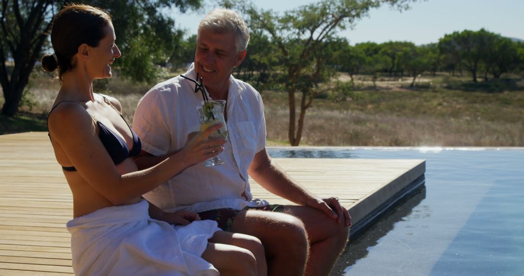 Happy Couple Relaxing by Pool in Sunlit Setting with Refreshing Drinks