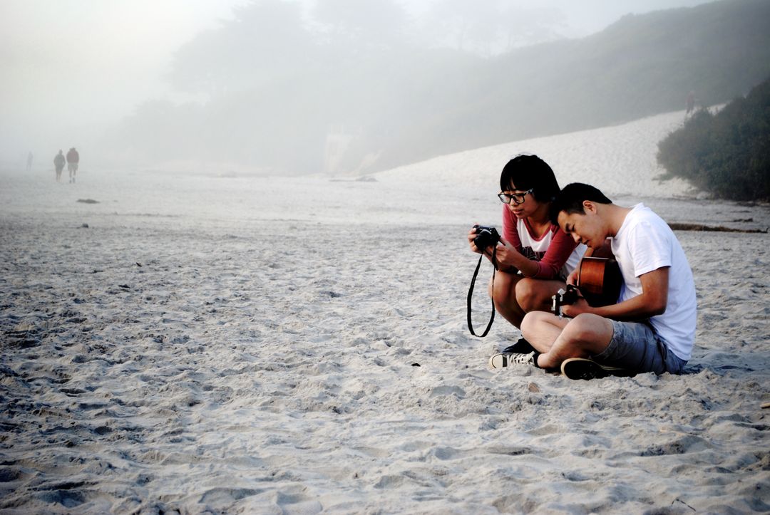 Young Friends Enjoying a Misty Beach Day with Camera and Guitar - Free Images, Stock Photos and Pictures on Pikwizard.com