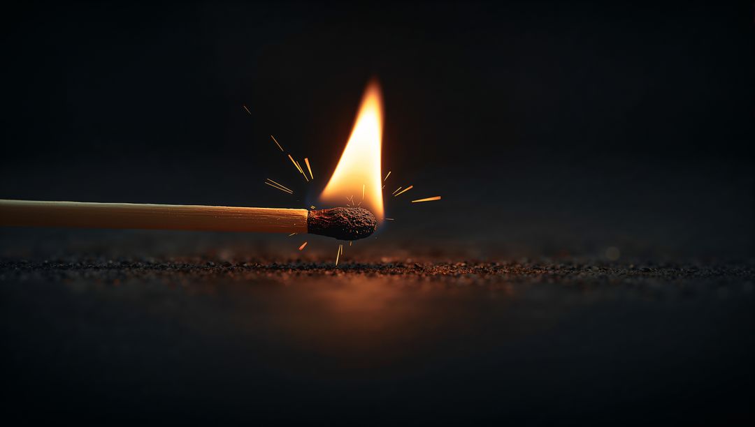 Closeup burning wooden match striking surface creating teardrop flame and flying sparks