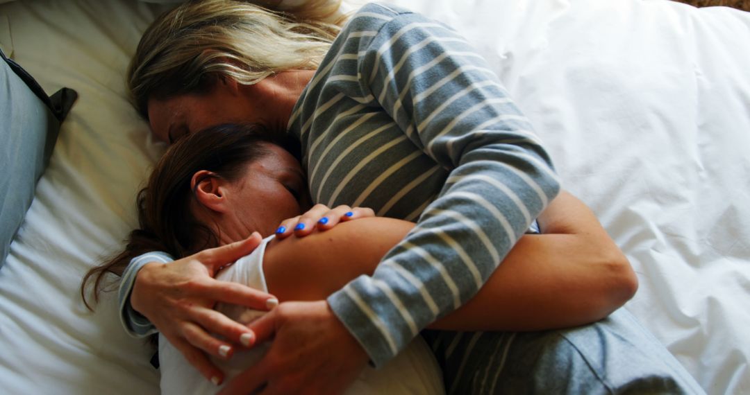 Comforting Hug between Two Women Lying on Bed in Striped Pajamas - Free Images, Stock Photos and Pictures on Pikwizard.com