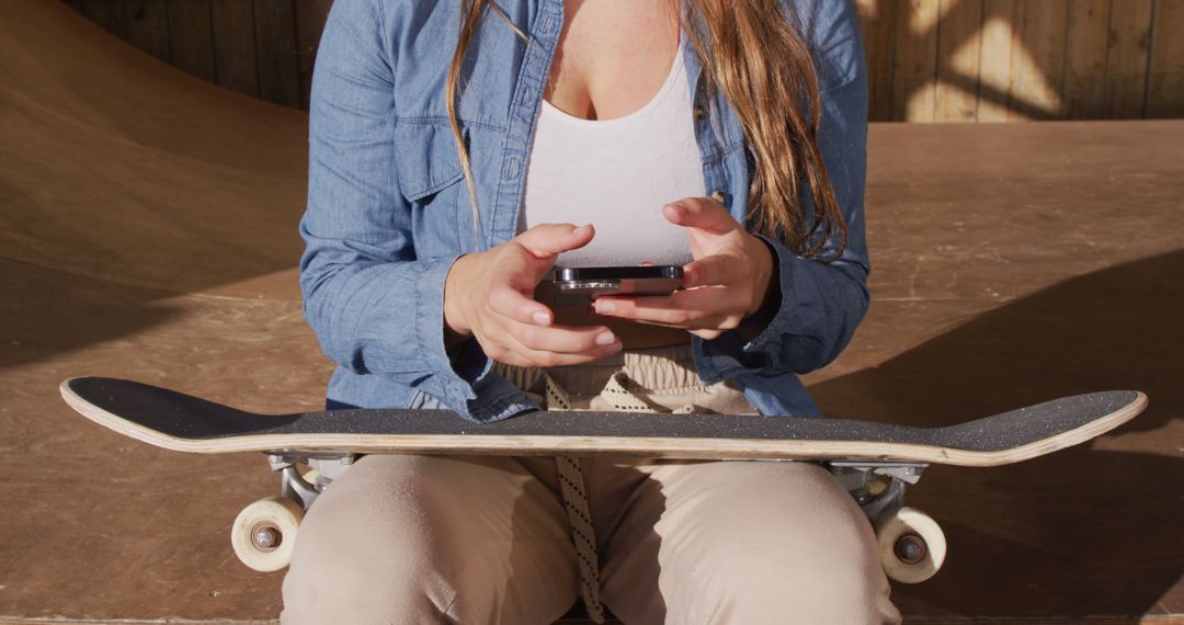 Young Woman Using Smartphone While Sitting with Skateboard - Free Images, Stock Photos and Pictures on Pikwizard.com