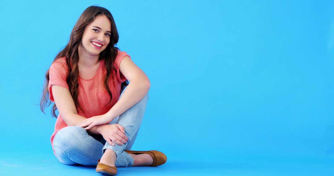 Smiling Young Woman Sitting on Blue Background in Casual Outfit - Free Images, Stock Photos and Pictures on Pikwizard.com