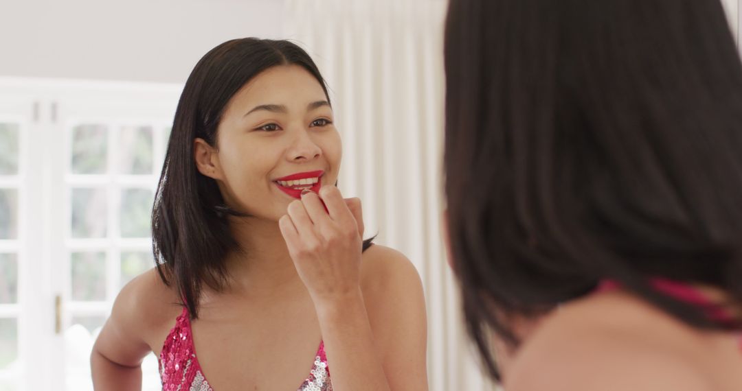 Image of biracial woman applying lipstick and dressed in pink dress - Free Images, Stock Photos and Pictures on Pikwizard.com