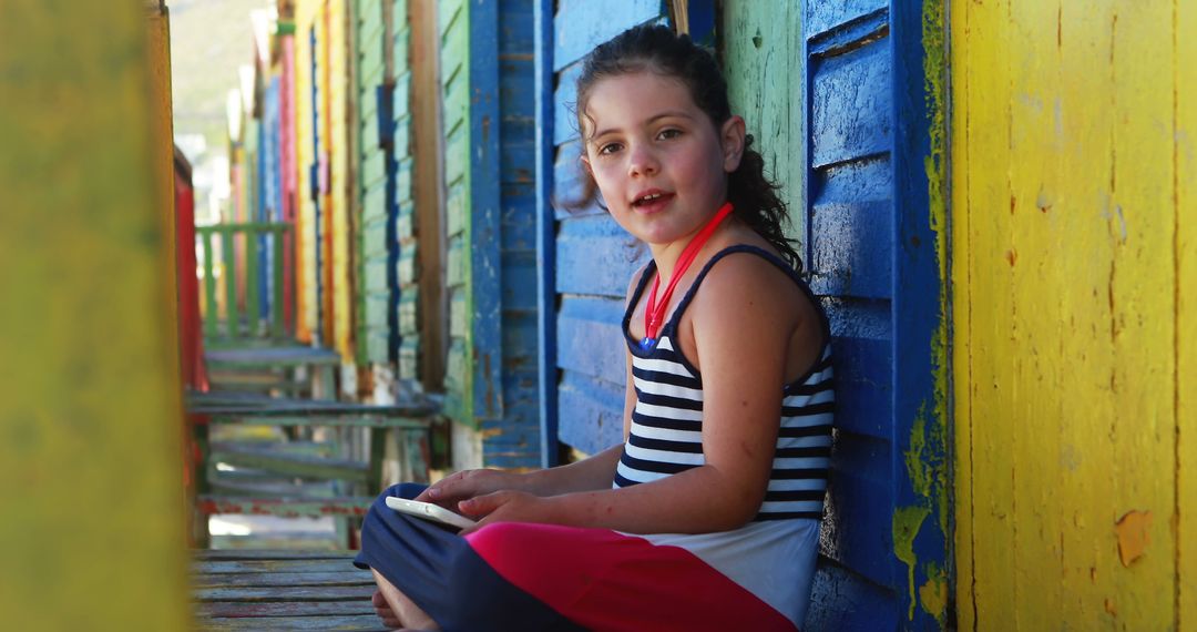 Adorable Girl Sitting by Colorful Beach Huts on Bright Day - Free Images, Stock Photos and Pictures on Pikwizard.com