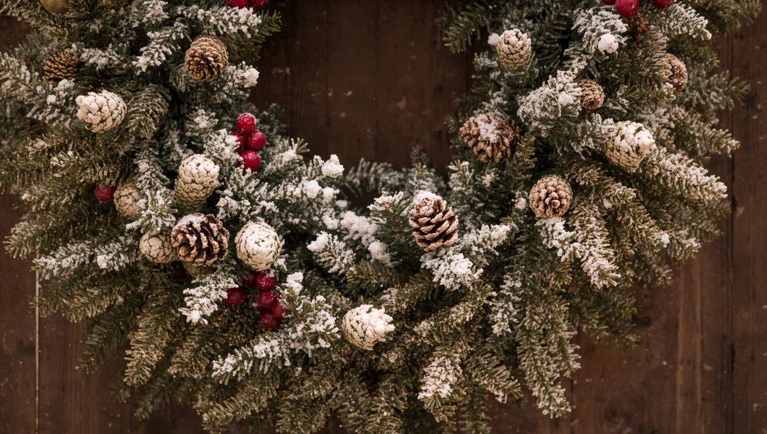 Snow-Dusted Fir Wreath Featuring Pine Cones and Red Berries on Rustic Wooden Door