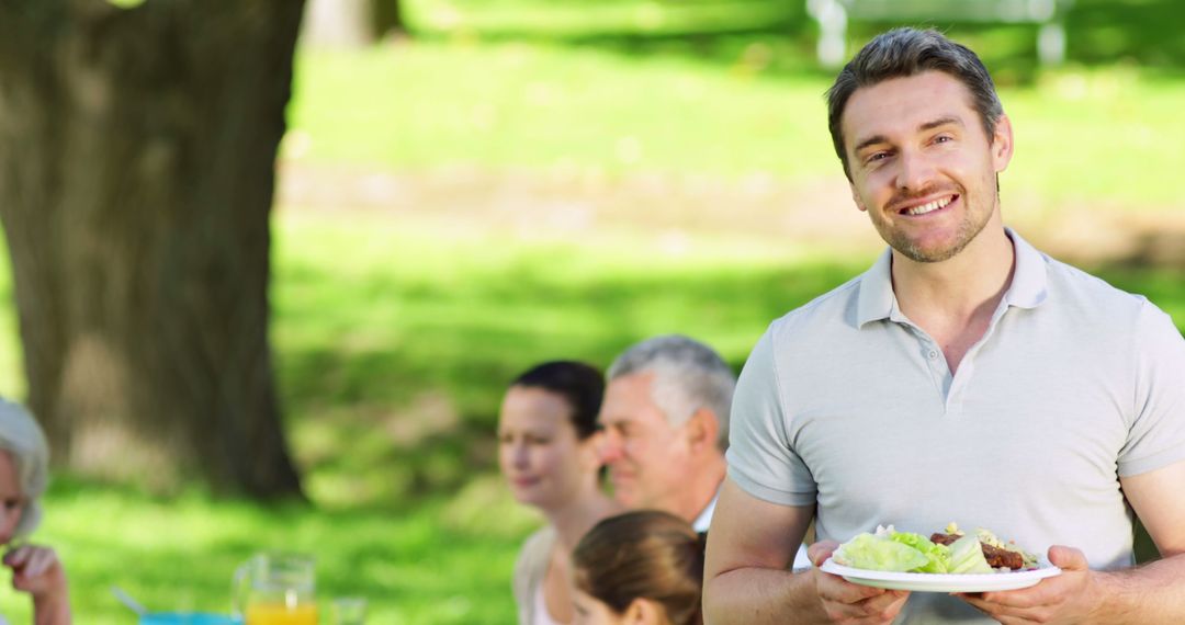 Smiling Man Holding Plate at Family Picnic in Park - Free Images, Stock Photos and Pictures on Pikwizard.com