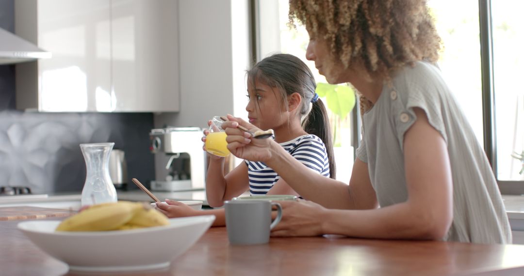 Biracial Mother and Daughter Enjoy Breakfast Cereal in Sunny Kitchen