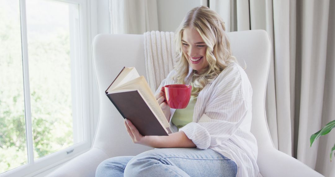 Smiling Woman Relaxing on Armchair with Book and Coffee by Sunny Window - Free Images, Stock Photos and Pictures on Pikwizard.com