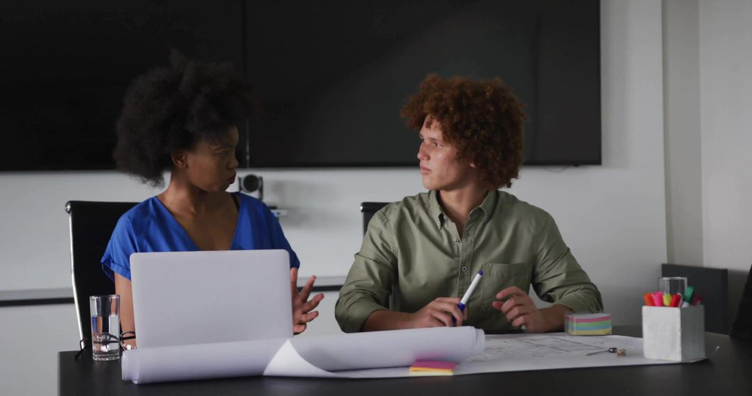 Young professionals discussing blueprints in modern boardroom for collaborative planning