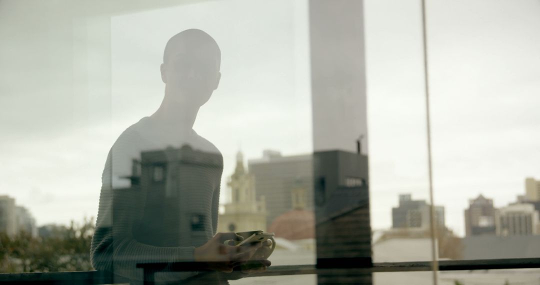 Reflective Silhouette of Person Holding Coffee Cup by Window with City View - Free Images, Stock Photos and Pictures on Pikwizard.com