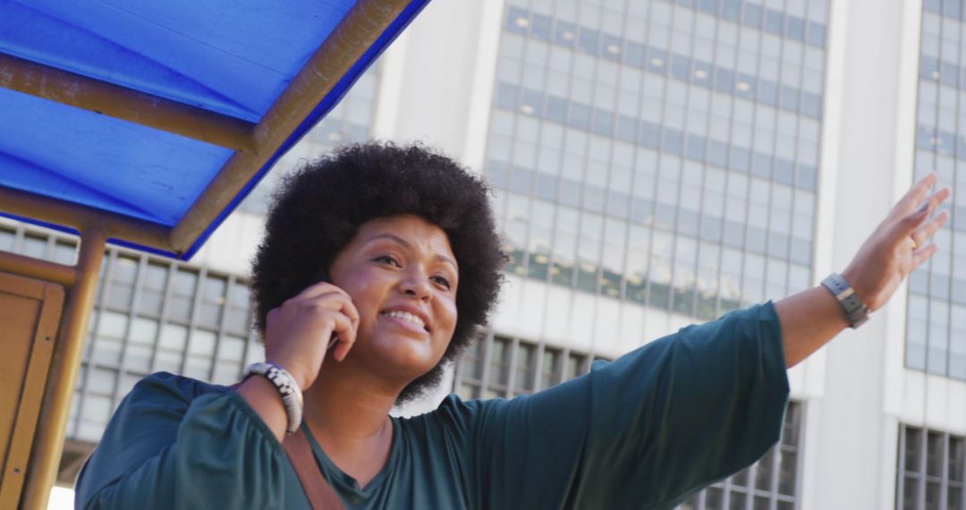 Smiling Woman Hailing Taxi and Talking on Smartphone in City