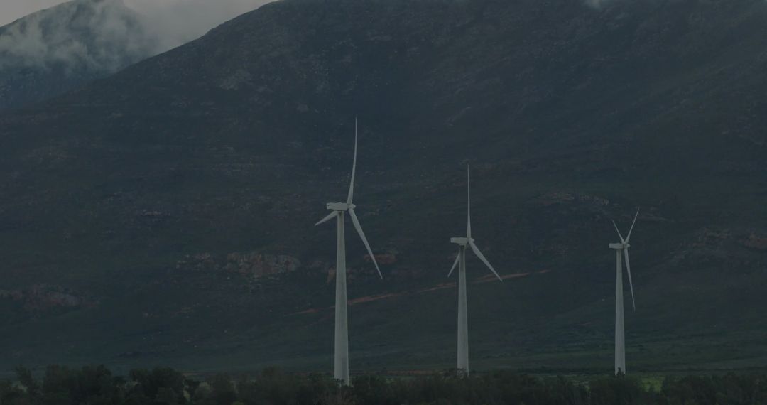 Wind turbines generating clean energy at misty mountain base in overcast rural landscape