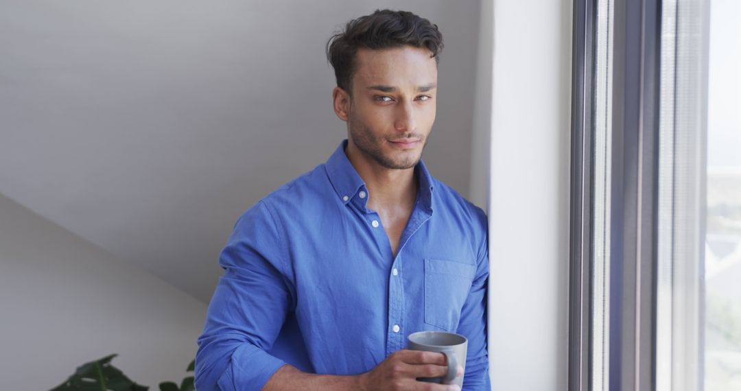 Confident Young Man Holding Coffee Mug by Window - Free Images, Stock Photos and Pictures on Pikwizard.com