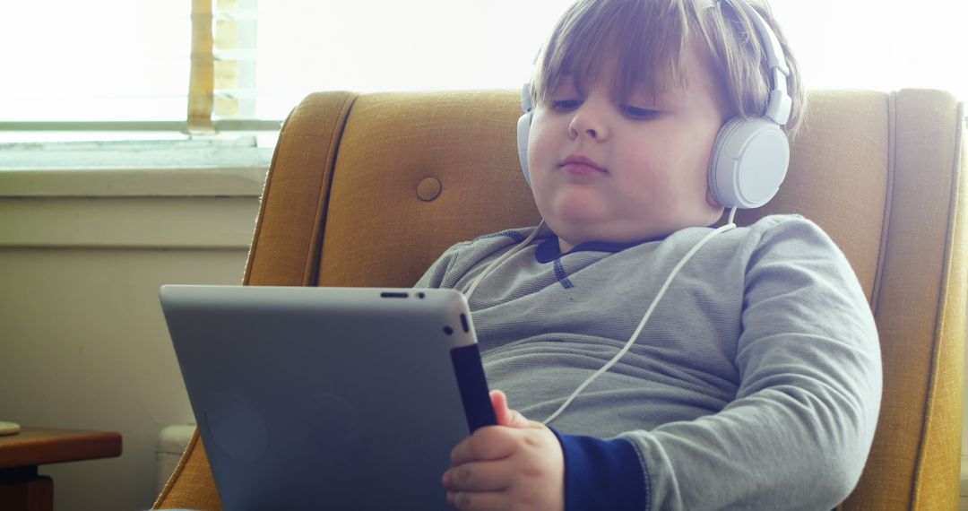 Young Child Enjoying Tablet With Headphones in Cozy Living Room - Free Images, Stock Photos and Pictures on Pikwizard.com