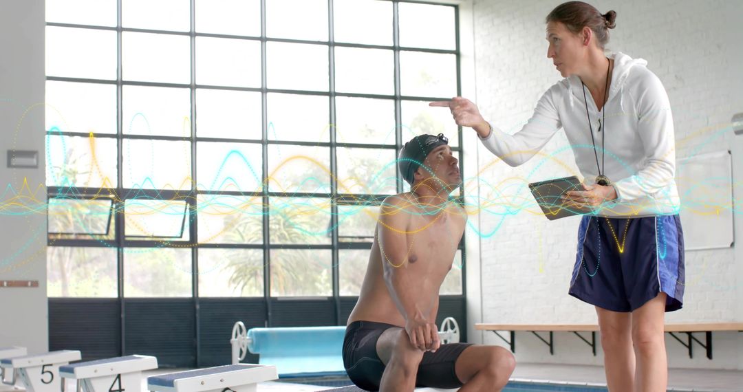 Female Swim Coach Pointing and Using Tablet Coaching Swimmer on Indoor Pool Deck